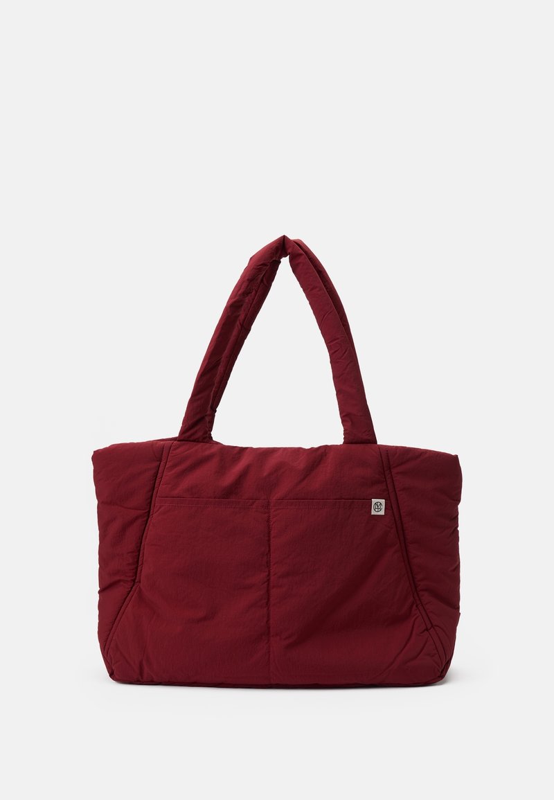 Sac cabas matelassé rouge avec deux anses, doté d'une poche avant et d'un tissu texturé. Forme rectangulaire avec des détails de couture.