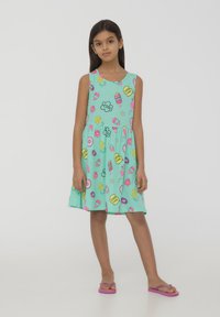 Un vestito senza maniche di colore verde menta con una stampa giocosa di gelati, frutta e fiori. Realizzato in tessuto morbido, presenta un design a gonna svasata.