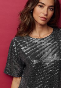 Top corto nero a maniche corte ricoperto di paillettes, con scollatura rotonda e una superficie lucida e texturizzata con accenti a forma di stella.