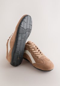 Baskets en daim marron avec un accent latéral blanc et une semelle en caoutchouc noire présentant un motif en chevrons. Bout arrondi et design à lacets.