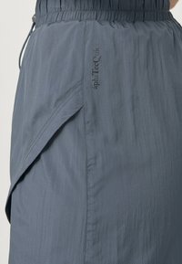 Grijze, lichte rok gemaakt van gladde stof, met een elastische tailleband, schuin aflopende zoom en een subtiel logo in donkergrijs.