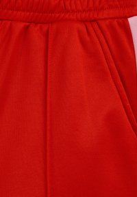 Gros plan sur un pantalon en tissu rouge avec une ceinture élastique et une poche latérale, montrant la texture et les détails des coutures.