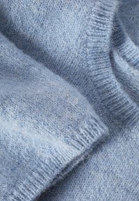 Tissu en laine tricotée bleu clair doux montrant une texture détaillée et des poignets côtelés, mettant en avant la chaleur et le confort du vêtement.