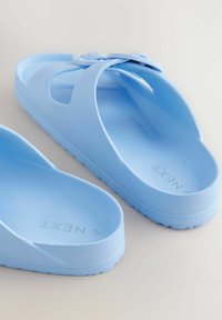 Helle blaue Plastikflip-Flops mit einem gerillten Riemen und einer strukturierten Sohle. Sie haben ein offenes Design und einen minimalistischen Stil.