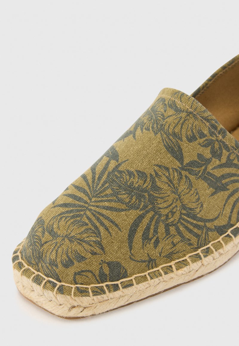 Scarpa slip-on espadrille in tessuto verde oliva con motivi a foglia scuri, dotata di suola in corda di juta e parte superiore liscia e texturizzata.