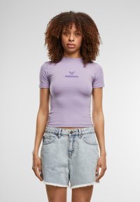 Violets krāsas pieguļošs T-krekls ar īsām piedurknēm un "felicious" logo centrā, savienots ar gaišiem džinsu šortiem ar saplēstu apakšmalu.