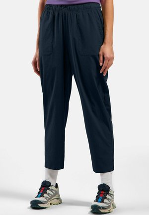 Marineblaue, leichte Hose mit elastischem Bund, zwei Seitentaschen und schmal zulaufenden Beinen. Getragen mit bunten Sportschuhen und weißen Socken.