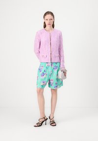 Lilla blondjakke med gullhardware, kombinert med blomstrende mintgrønne shorts og svarte stiletthæler. Sølvveske fullfører antrekket.