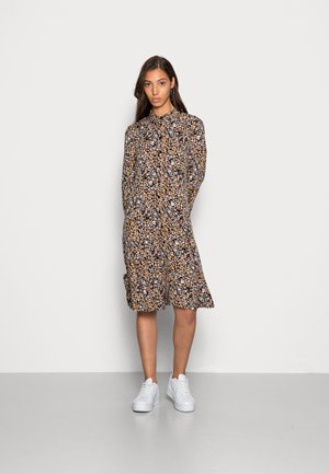 Vestido preto com padrão floral colorido, mangas longas, frente com botões e comprimento até ao joelho, combinado com ténis brancos. Textura de tecido suave.