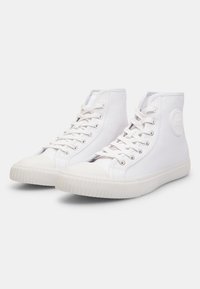 Adidași înalți din pânză albă, cu vârf rotunjit, șireturi plate și talpă din cauciuc texturat. Prezintă un accent cu logo circular pe lateral.