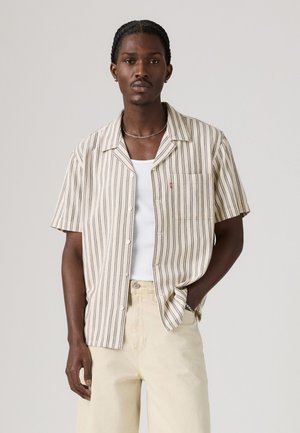 Short-sleeve shirt in off-white with vertical navy stripes. Button-up front, single chest pocket, casual fit, worn over a white tank top.