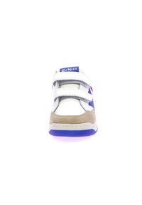 Sneaker bianco e blu con cinturini in velcro, dettagli in suede beige, texture in pelle liscia e collare imbottito, con una suola viola.
