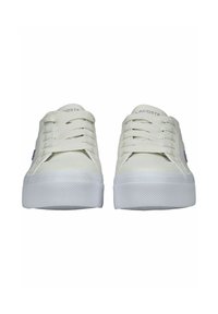 Białe trampki na sznurowadła wykonane z gładkiego materiału, z teksturowaną podeszwą i subtelnym fioletowym logo Lacoste po boku. Prosty, niskoprofilowy design.