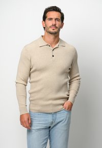 Beige gestreiftes Langarm-Polohemd mit einem Button-Down-Kragen und drei schwarzen Knöpfen, kombiniert mit hellblauen Jeans.