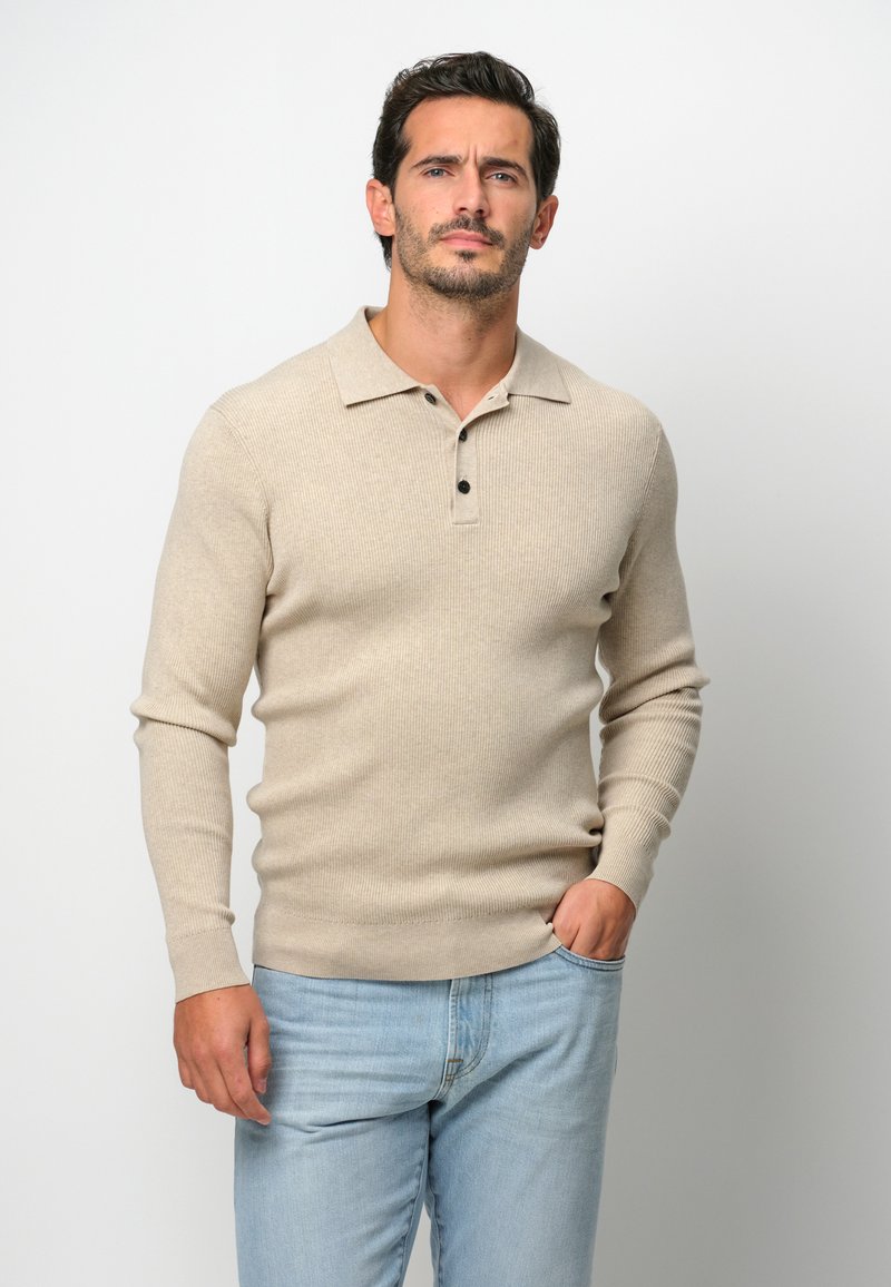 Beige gestreiftes Langarm-Polohemd mit einem Button-Down-Kragen und drei schwarzen Knöpfen, kombiniert mit hellblauen Jeans.