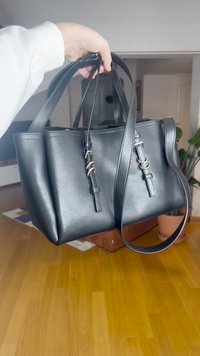 Fekete bőr válltáska dupla felső fogantyúval, oldalsó díszítésekkel és fém részletekkel. Simás tapintású; téglalap alakú.