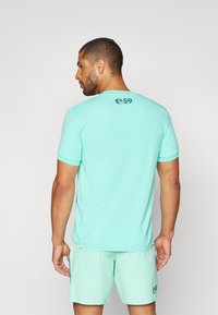 Light turquoise athletic shirt with short sleeves, textured fabric, and a logo printed on the upper back; paired with matching shorts.