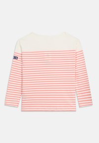 Λευκό πουκάμισο με μακριά μανίκια, διακοσμημένο με οριζόντιες κοραλλένιες ρίγες και μικρό σκούρο μπλε λογότυπο στο αριστερό μανίκι, απλωμένο επίπεδα σε λευκό φόντο.