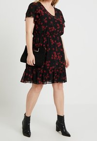 Svart blommig klänning med röda rosor, volangärmar, knälång, åtsittande midja, kombinerad med en svart clutch och ankelboots.