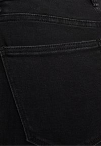 Jeans de mezclilla negra con una textura suave, que cuentan con dos bolsillos traseros y costuras en contraste. El diseño destaca una forma ajustada.