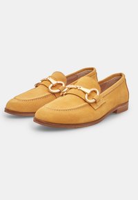 Suedes loafers spilgtā dzeltenā krāsā ar noapaļotu purngalu, dekoratīvu zeltainu aparatūru un kontrastējošu šuvumu. Plakana koka zole.