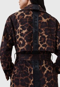 Cappotto trench stampa leopardata in marrone e nero, con vita smalianata, ampio colletto e un accento nero con marchio lungo la schiena.