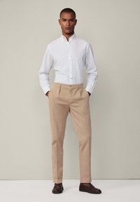 Camicia con bottoni a quadri blu chiaro e bianchi, abbinata a pantaloni beige e mocassini marroni scuri.