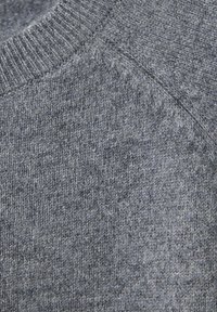 Gros plan d'un pull en laine gris tricoté montrant un col côtelé et un motif de maille texturé.