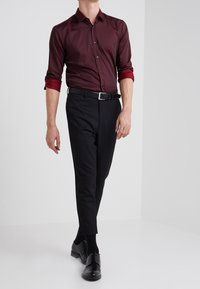Camisa burdeos de botones con mangas enrolladas, combinada con pantalones negros ajustados y zapatos negros. Tejido suave; diseño entallado.