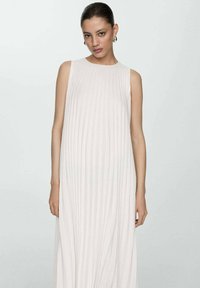Rochie plisată de culoare deschisă, fără mâneci, cu o siluetă fluidă și textură netedă, având un decolteu rotund și deschideri laterale.
