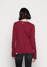Långärmad skjorta i burgundy-randig med rundad halsringning, en dekorativ knapp på baksidan och en något avslappnad passform.