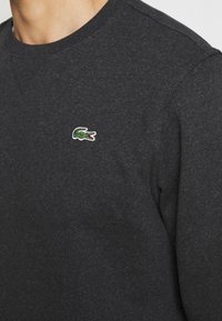 Mörkgrå långärmad skjorta i en texturerad bomullsblandning, med en liten grön och vit broderad krokodil-logotyp på vänster bröst.