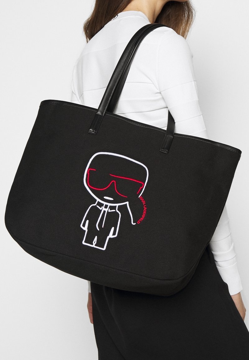 Svart canvas-tygväska med svarta läderremmar. Har ett broderat motiv i vitt och rött som tillför ett lekfullt designelement.