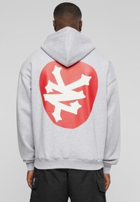 Graue Kapuzenjacke mit einem großen roten runden Grafikdesign und einem weißen sternförmigen Motiv auf dem Rücken. Aus Baumwollmaterial mit lockerer Passform.