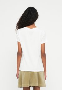White cotton t-shirt with short sleeves and a V-neck, worn with a khaki corduroy skirt featuring pleats and a hemline at mid-thigh.