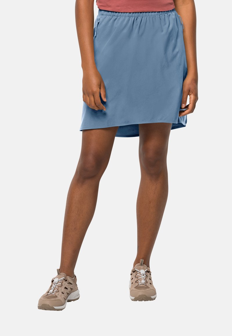 Blauwe sportrok met een elastische tailleband en zijzakken met rits, gedragen met beige sneakers. Zachte stof en knielange ontwerp.