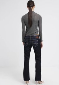 Jeans svasati in denim blu scuro con toppa posteriore in pelle, tasche posteriori ricamate e vita media. Abbinati a un top grigio a coste.