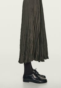 Ciemna plisowana spódnica o zwiewnym kroju, zestawiona z czarnymi prążkowanymi skarpetkami i błyszczącymi czarnymi oksfordami sznurowanymi.