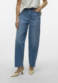 Jeans de mezclilla de corte recto y tiro alto, en un tono azul claro. Cuentan con pasadores para cinturón, bolsillos delanteros y un sutil desgaste. Un par de zapatos de tacón color beige.