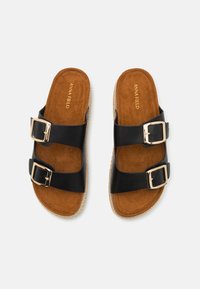 Black slide sandals with two wide straps, gold metal buckles, and a tan suede footbed. Braided jute textured sole adds detail.