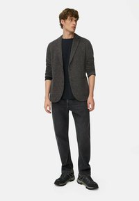 Dunkelgrauer Blazer aus strukturiertem Stoff, mit einem einzigen Knopfverschluss, kombiniert mit einem schwarzen T-Shirt und dunklen Jeans, abgerundet mit schwarzen Schuhen.