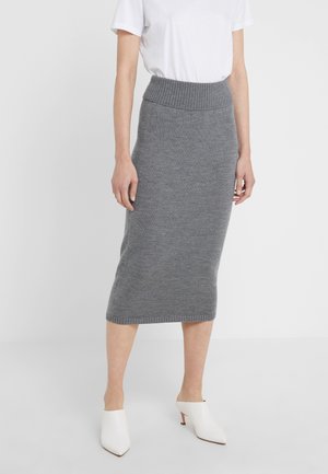 Grå strikket midi-nederdel med ribstrikket taljebånd, glat tekstur og en tætsiddende silhuet. Kombineret med hvide mules med åben tå.