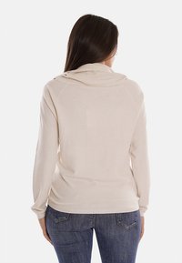 Pullover beige a maglia con scollo a cowl, maniche lunghe e orlo aderente, abbinato a jeans in denim blu scuro. Texture liscia.