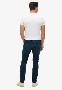 T-shirt ajusté en coton blanc associé à un jean en denim bleu foncé. Le jean présente des poches arrière et un design à jambe droite, agrémenté de baskets claires.