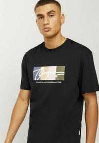 Camiseta de algodón negra con un gráfico rectangular que presenta rayas de colores y texto en blanco, incluyendo "Presentado por Jack&Jones©1990."