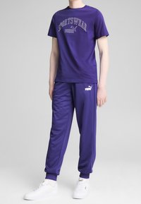 Purple sportswear set featuring a crew-neck t-shirt with "SPORTSWEAR" text and matching sweatpants, both made of soft fabric, with elastic cuffs.