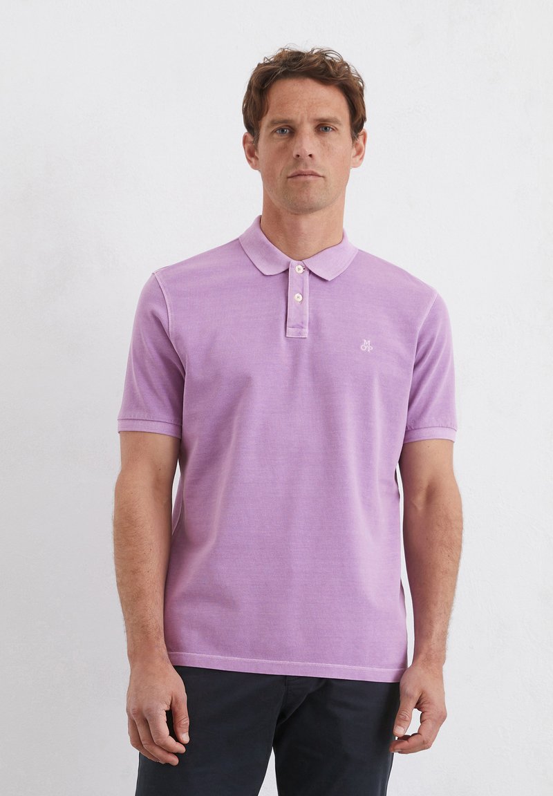 Jasnofioletowa koszulka polo o miękkiej strukturze, krótki rękaw, zapinany kołnierzyk oraz małe logo na lewej piersi; klasyczny krój.