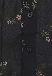 Schwarze Stoffbluse mit pinkem Blumenmuster, mit einer Reihe von zwei schwarzen Knöpfen in der vorderen Mitte und einem leichten, strukturierten Finish.