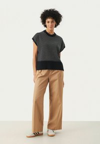 Top de manga corta a rayas blancas y negras con dobladillo acanalado, combinado con pantalones de pierna ancha en color beige y zapatillas grises con rayas negras.