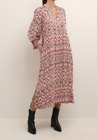 Long, pink, and green patterned dress with a collar, long sleeves, and side slits. Worn with black ankle boots. Soft fabric with a flowy design.